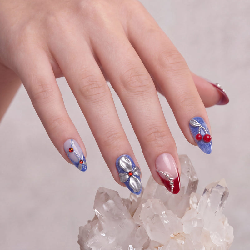 Rebel Cherry handmade press-on nails on a hand model with blue accents, silver bows, red cherry charms, and red French tips