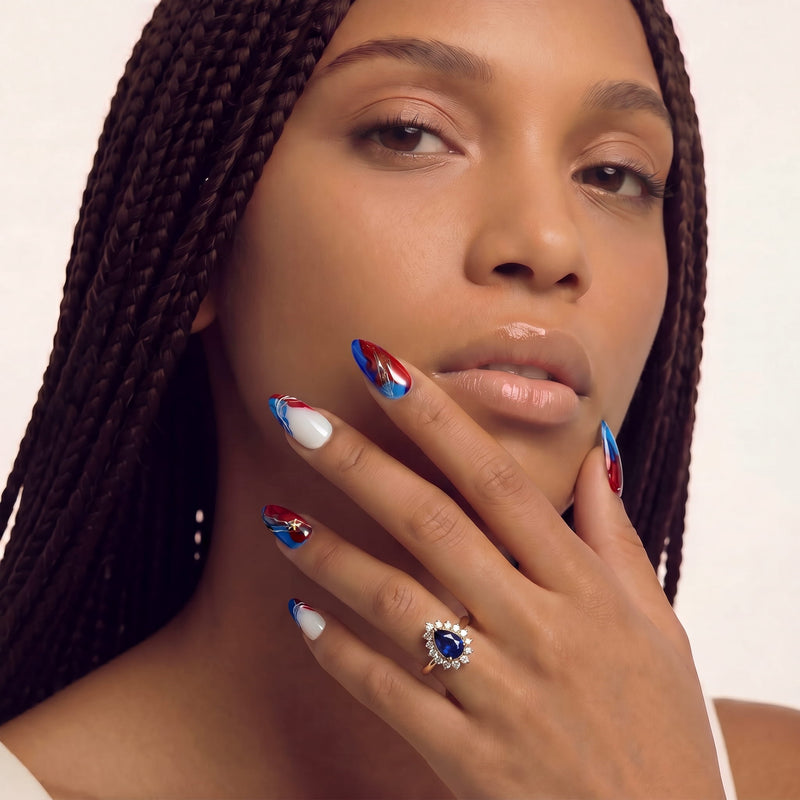 Portrait of a hand model wearing red, white, and blue press-on nails with a jeweled ring.