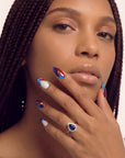 Portrait of a hand model wearing red, white, and blue press-on nails with a jeweled ring.