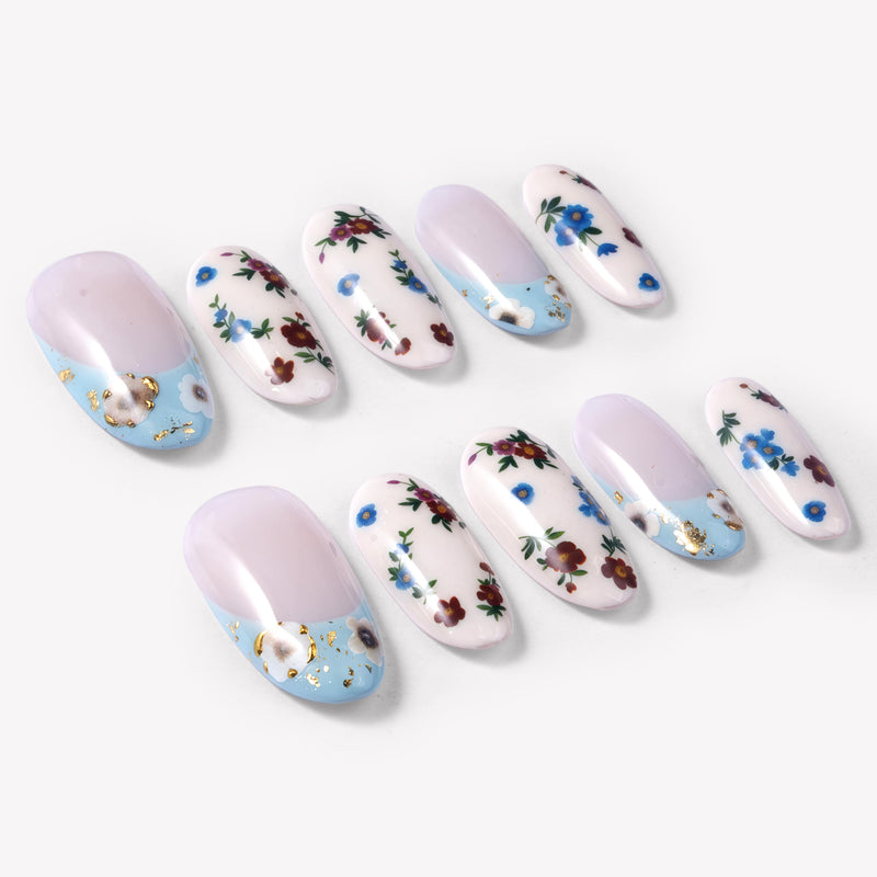 Angled flat lay of Retro Pastoral press-on nails with pale pink bases, light blue curved tips, gold foil accents, and red and blue floral designs