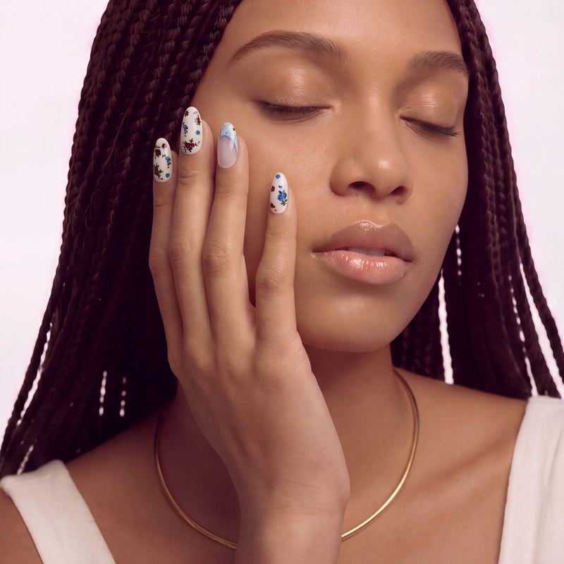 Face close-up hand model wearing Retro Pastoral press-on nails with pale pink bases, light blue curved tips, and tiny red and blue floral designs