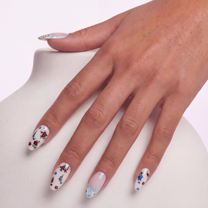 Hand model wearing Retro Pastoral press-on nails with pale pink bases, light blue curved tips, gold foil accents, and tiny floral designs