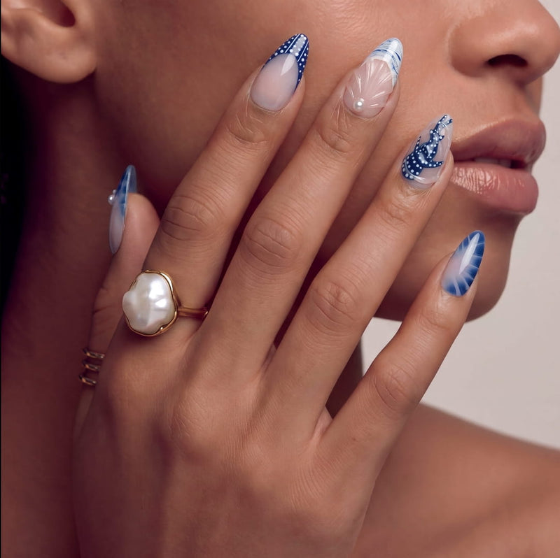 Face close-up of a hand model wearing blue and white floral press-on nails with a pearl ring.