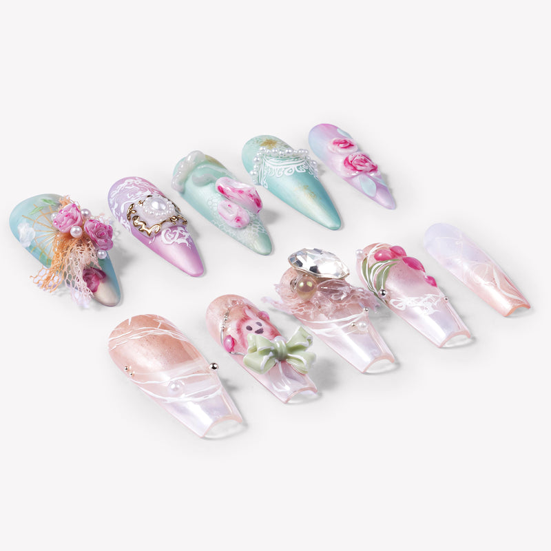 Angled flat lay of Rococo Reverie press-on nails with pastel blue and pink bases, 3D roses, pearls, lace details, bows, and rhinestones
