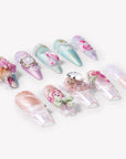 Angled flat lay of Rococo Reverie press-on nails with pastel blue and pink bases, 3D roses, pearls, lace details, bows, and rhinestones