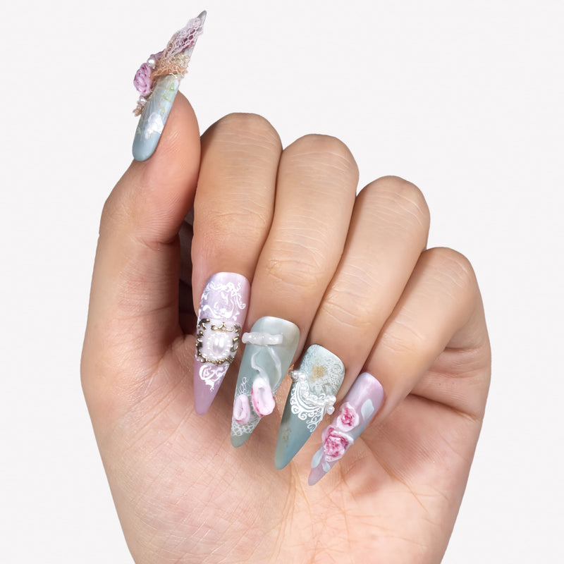 Hand model wearing Rococo Reverie press-on nails with pastel blue and pink bases, 3D roses, pearls, lace details, and bows