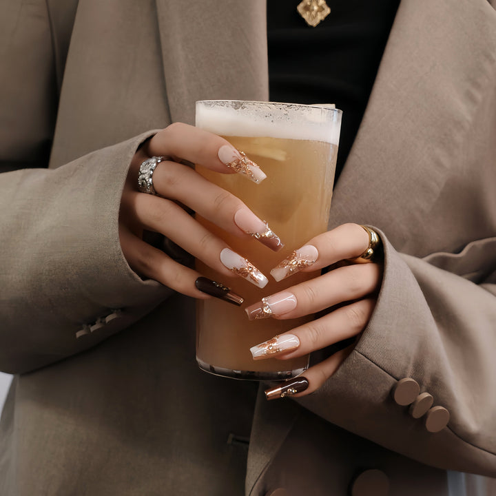 Hand model holding a drink while wearing Rosegold Flutter press-on nails with glossy nude, white, and burgundy designs plus rosegold butterfly accents