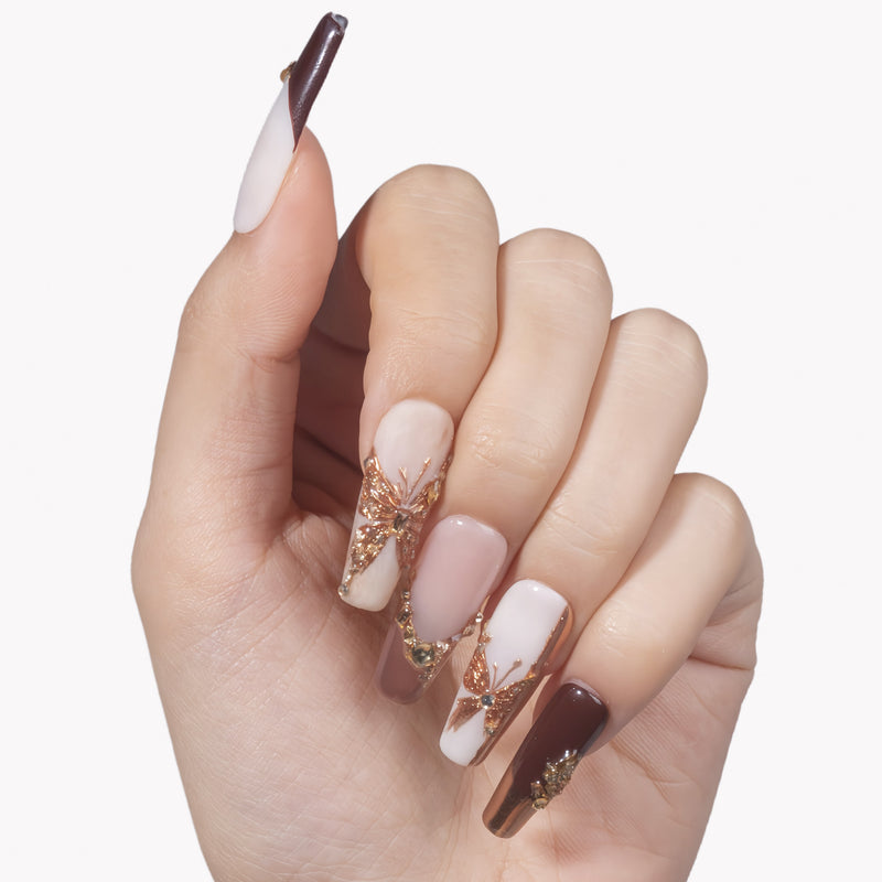 White background hand model wearing Rosegold Flutter press-on nails with burgundy tips, soft pink accents, rosegold butterfly charms, and rhinestones