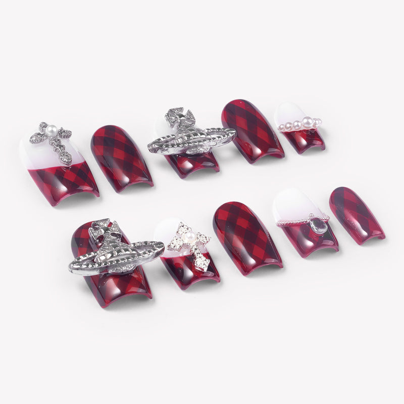 Angled flat lay of Royal Rebellion press-on nails with red black argyle pattern, white gradient bases, silver orb charms, pearls, and rhinestones