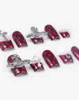 Angled flat lay of Royal Rebellion press-on nails with red black argyle pattern, white gradient bases, silver orb charms, pearls, and rhinestones