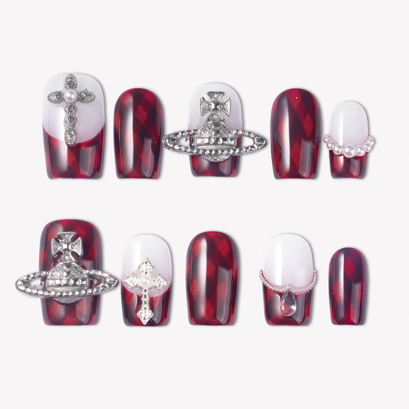 Royal Rebellion press-on nails with red black argyle pattern, white gradient bases, silver orb charms, cross charm, pearls, and rhinestones