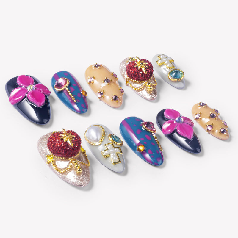 Angled flat lay of Saint of Desire press-on nails with pink flowers, red heart charms, gold cross details, pearls, and gemstones