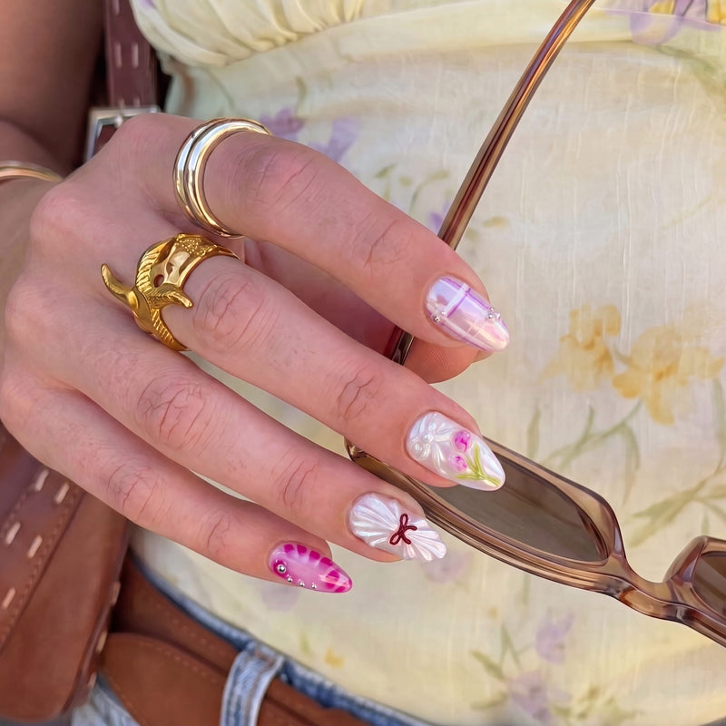 Close-up of Sakura Whisper pearly floral press-on nails with pink plaid, tulips and red bow details while holding sunglasses
