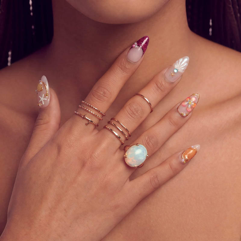Hand model wearing ocean-themed press-on nails with seashell, starfish, and flower accents.