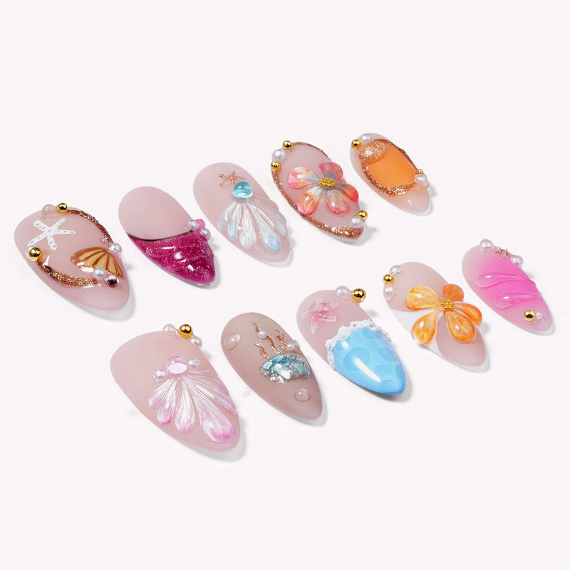 Individual ocean-colored press-on nails arranged on a white background with shells, flowers, and pearl accents.