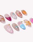 Individual ocean-colored press-on nails arranged on a white background with shells, flowers, and pearl accents.