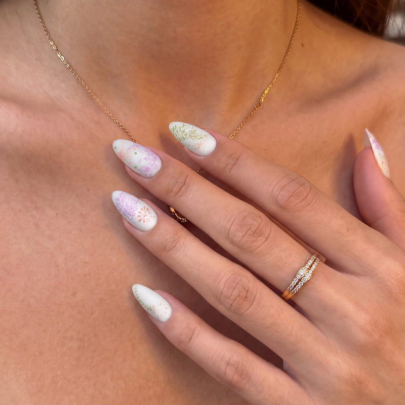Close-up of Secret Garden press-on nails with pastel floral details against a necklace and bare skin