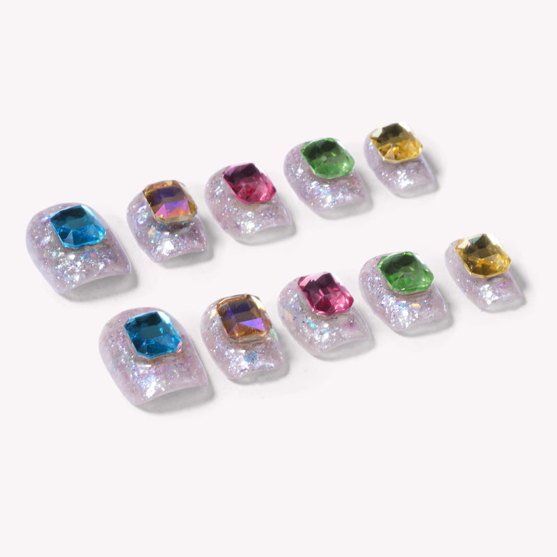 Detail layout of silver holographic glitter press-on nails with multicolor emerald-cut rhinestones on a white background.