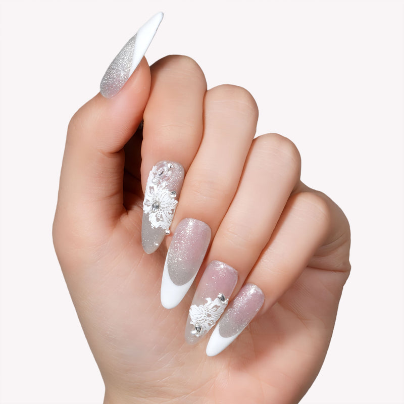 Close-up of a hand model wearing Snowlace Whisper press-on nails with silver shimmer, white lace accents, and crystal details