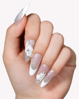 Close-up of a hand model wearing Snowlace Whisper press-on nails with silver shimmer, white lace accents, and crystal details