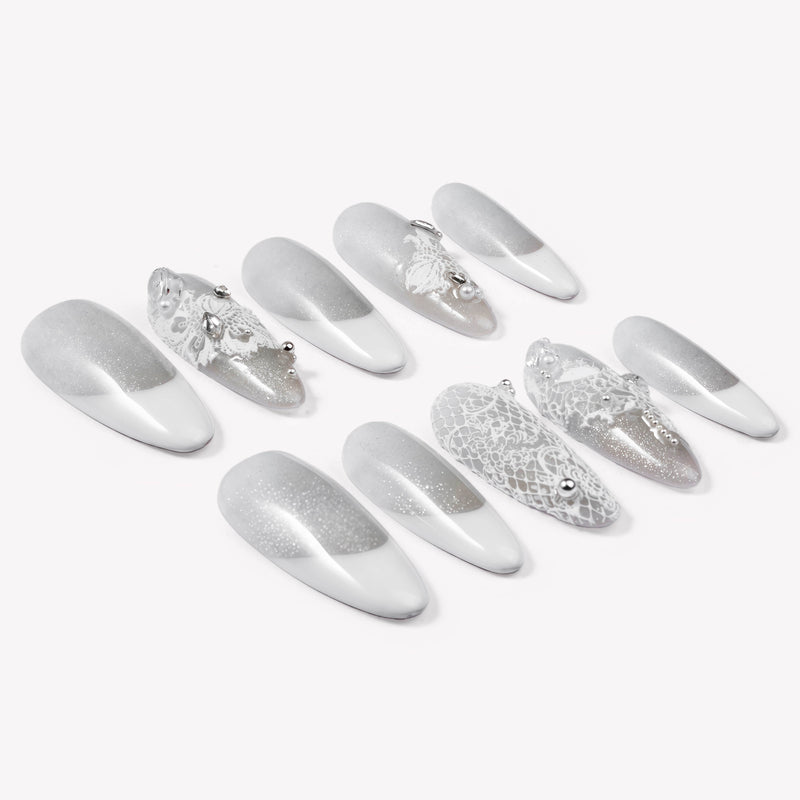 Flat lay of Snowlace Whisper press-on nails with silver shimmer, white lace accents, and crystal embellishments arranged in two rows