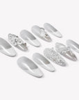 Flat lay of Snowlace Whisper press-on nails with silver shimmer, white lace accents, and crystal embellishments arranged in two rows
