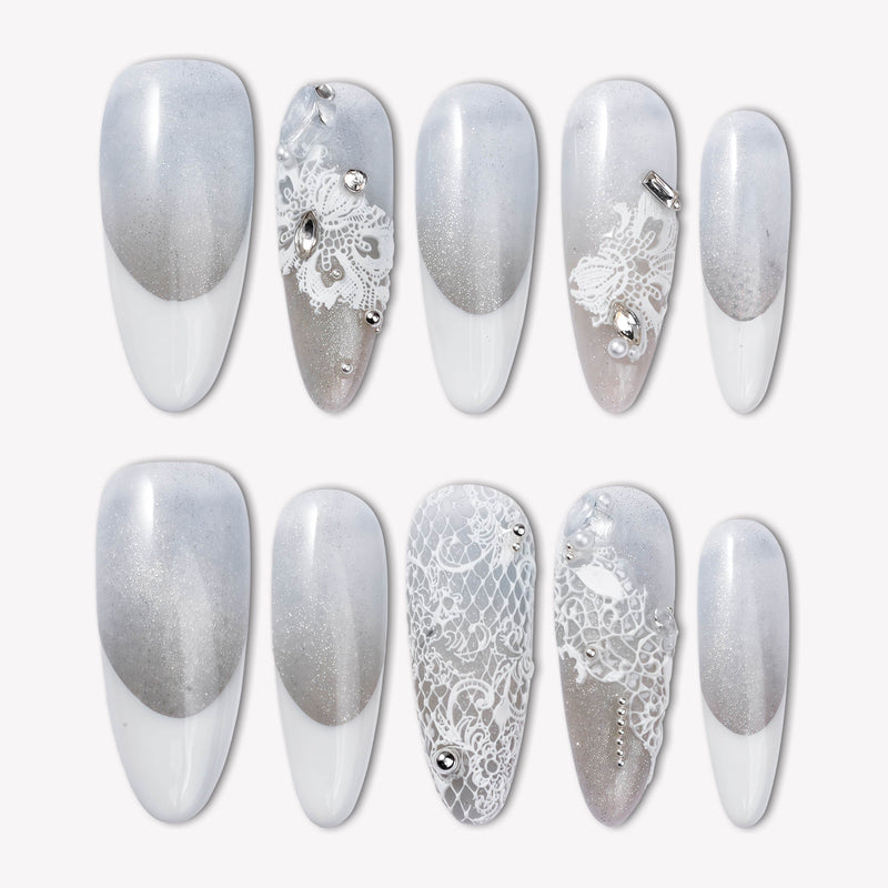 Flat lay of Snowlace Whisper press-on nail swatches with silver shimmer, white lace accents, and crystal embellishments