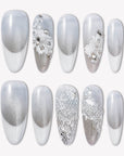 Flat lay of Snowlace Whisper press-on nail swatches with silver shimmer, white lace accents, and crystal embellishments