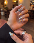 Cafe lifestyle view of Solar Pulse orange, pale blue and sculpted silver chrome press-on nails on a hand model