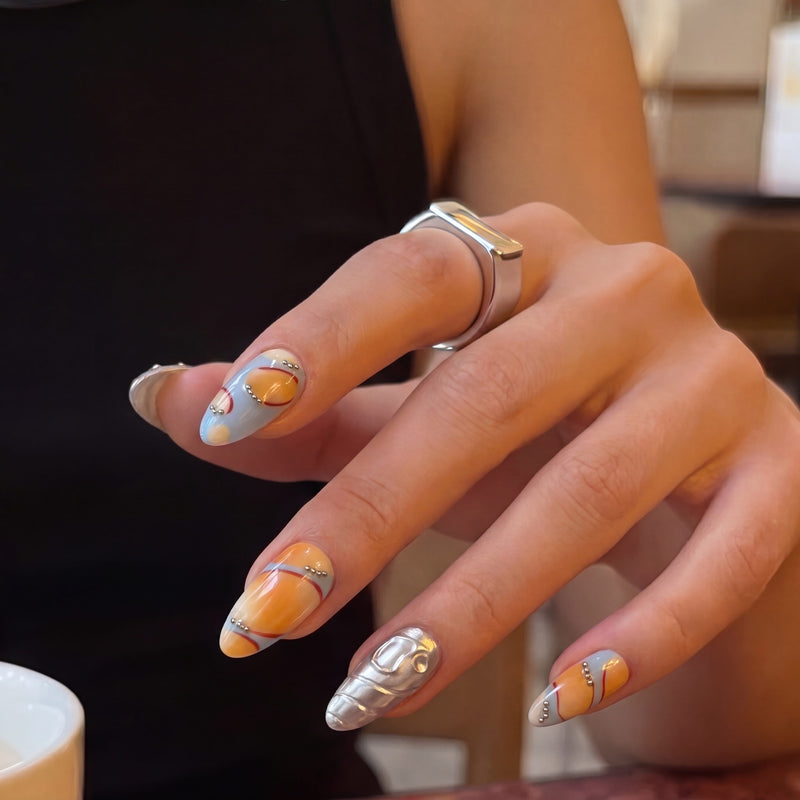 Hand model wearing Solar Pulse orange and pale blue almond press-on nails with silver chrome accent nails