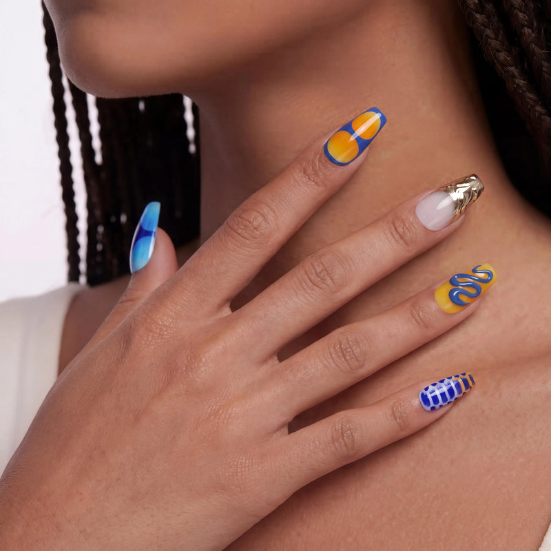 Hand model wearing Solar Tide press-on nails with blue and orange wave art, metallic gold accents, and glossy finish