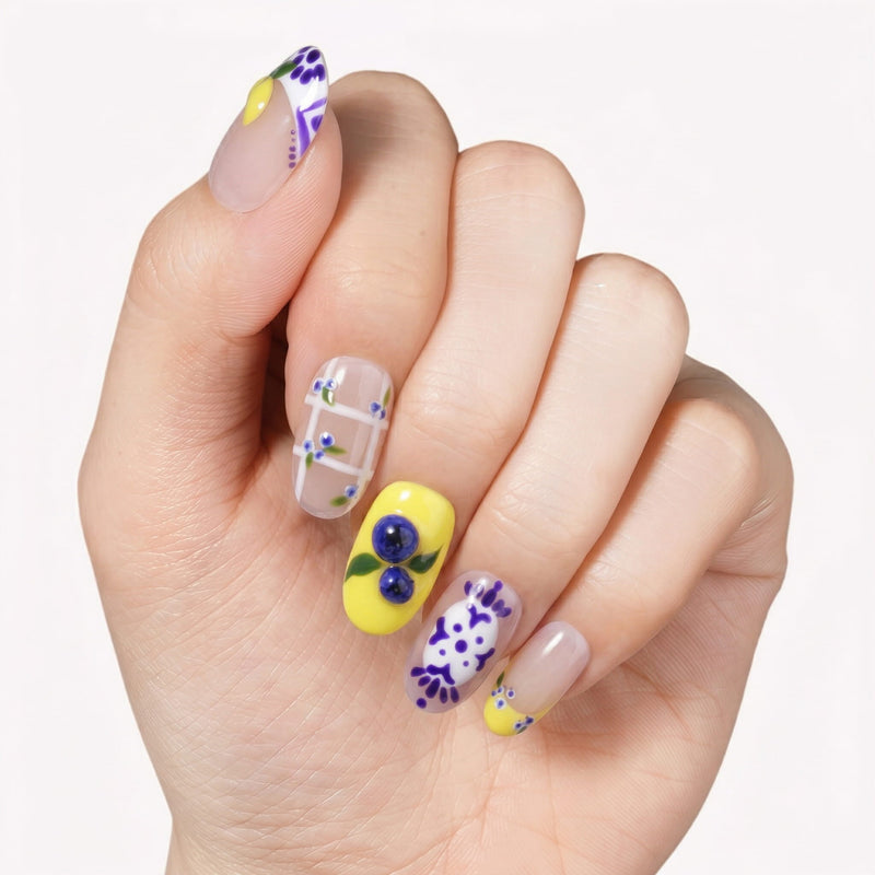 Close-up of a hand wearing colorful floral and fruit-inspired press on nails on a white background