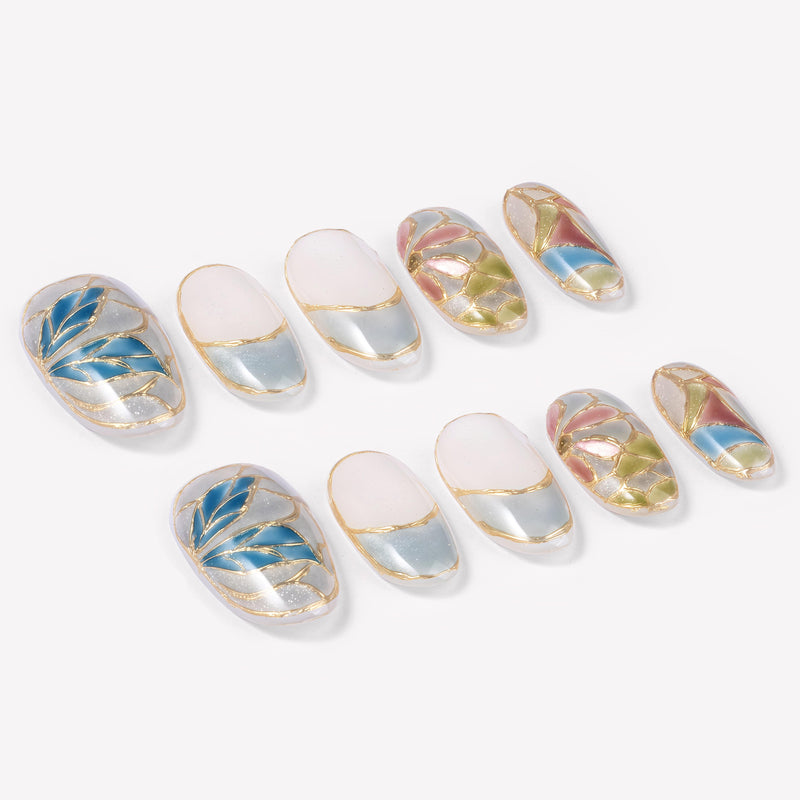 Angled flat lay of Stained Glass Leaves press-on nails with translucent blue, green, pink, and cream panels, raised gold leaf outlines, and shimmer finish