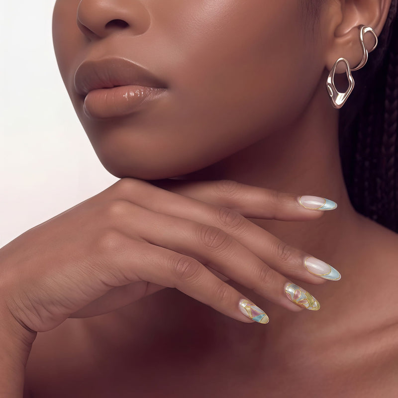 Hand model wearing Stained Glass Leaves press-on nails with blue and cream French tips, translucent leaf panels, raised gold outlines, and glossy finish