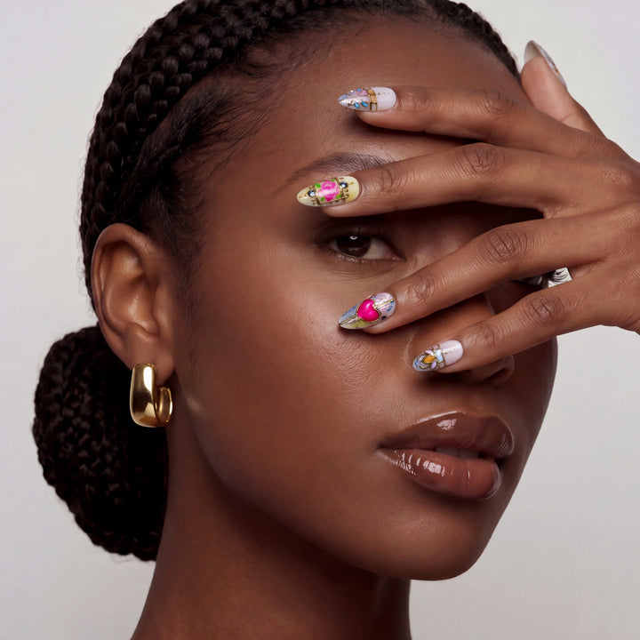 Portrait of a woman wearing colorful stained glass press on nails and posing with her hand over her face