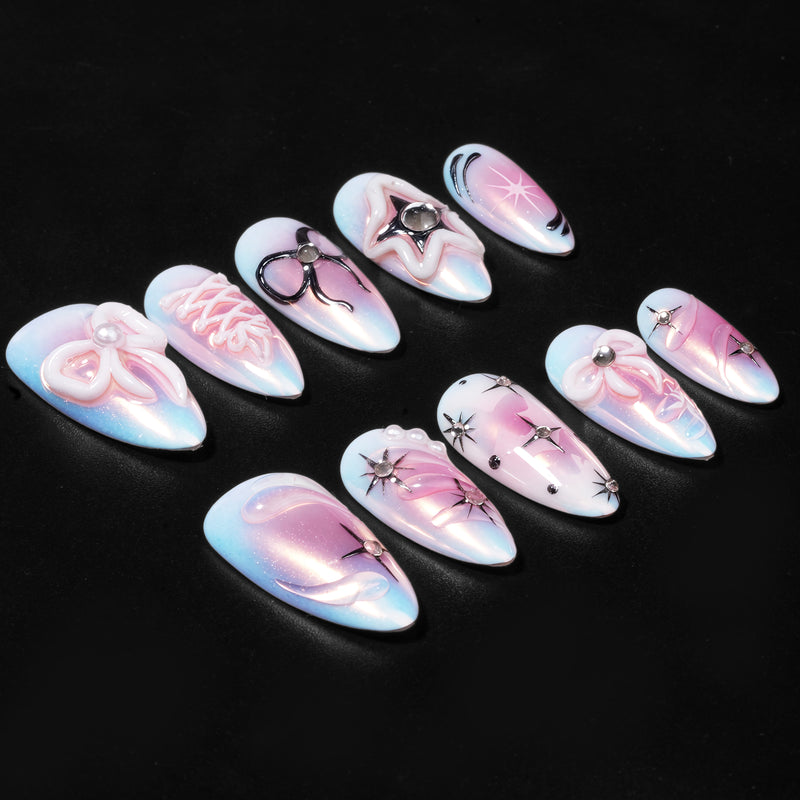 A set of iridescent blue and pink press-on nails with bows, stars, and rhinestone accents on a black background