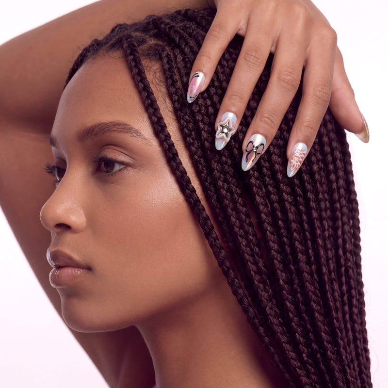 A side profile hand model wearing iridescent press-on nails with bows, stars, and chrome accents