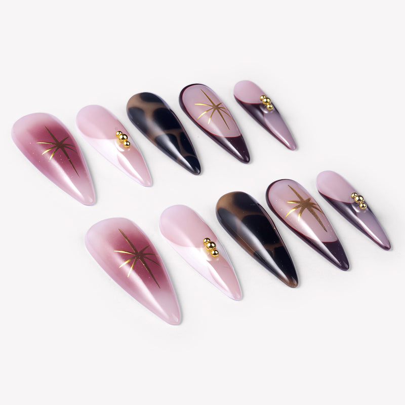 Angled flat lay of Starlit Mocha press-on nails with pink shimmer, black mocha cat-eye accents, gold starbursts, and bead details