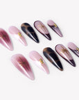 Angled flat lay of Starlit Mocha press-on nails with pink shimmer, black mocha cat-eye accents, gold starbursts, and bead details