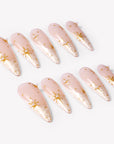 Angled flat lay of Starlit Veil press-on nails with sheer pink bases, white misty tips, gold starbursts, tiny gold studs, and pearl accents