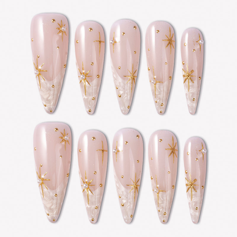 Starlit Veil press-on nails with sheer pink bases, white misty tips, gold starbursts, tiny gold studs, and pearl accents