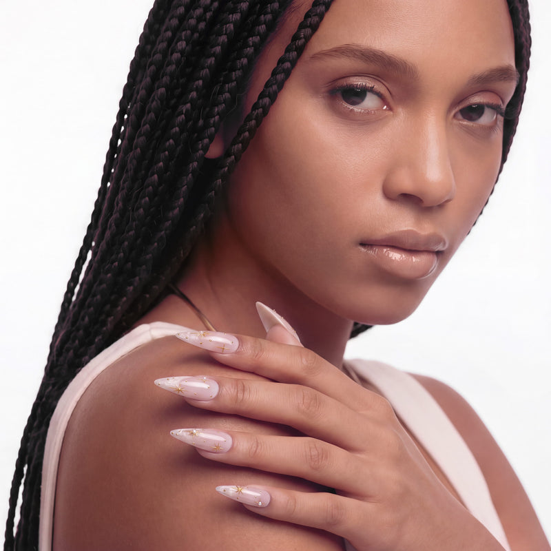 Portrait hand model wearing Starlit Veil press-on nails with sheer pink bases, white misty tips, gold starbursts, and pearl accents
