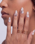 Side face close-up hand model wearing Starlit Whisper press-on nails with translucent nude pink bases, white star patterns, silver star accents, and silver beads