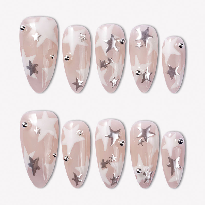 Starlit Whisper press-on nails with translucent nude pink bases, white star patterns, silver star accents, silver beads, and glossy almond shapes