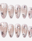 Starlit Whisper press-on nails with translucent nude pink bases, white star patterns, silver star accents, silver beads, and glossy almond shapes