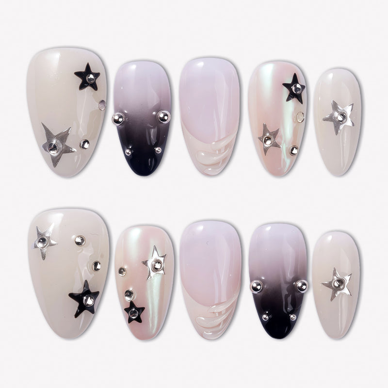 Stellar Muse press-on nails with black and silver star charms, rhinestones, silver beads, glossy nude pink bases, and black gradient accents