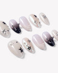 Flat lay of Stellar Muse press-on nails with black and silver star charms, rhinestones, silver beads, glossy nude pink bases, and black gradient accents