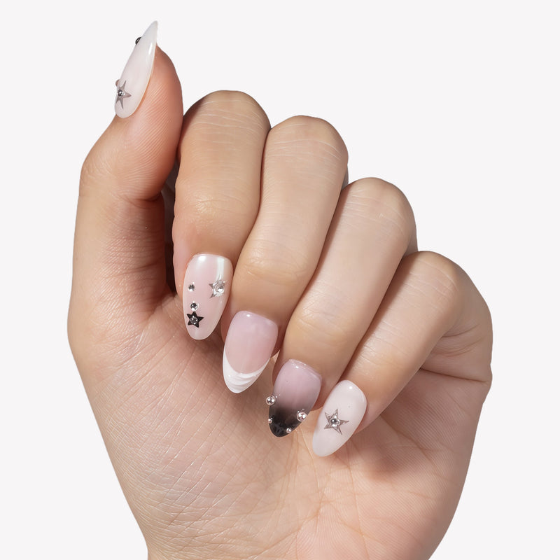 Hand model wearing Stellar Muse press-on nails with black and silver star charms, rhinestones, silver beads, nude pink bases, and soft black gradient accents