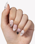 Hand model wearing Stellar Muse press-on nails with black and silver star charms, rhinestones, silver beads, nude pink bases, and soft black gradient accents