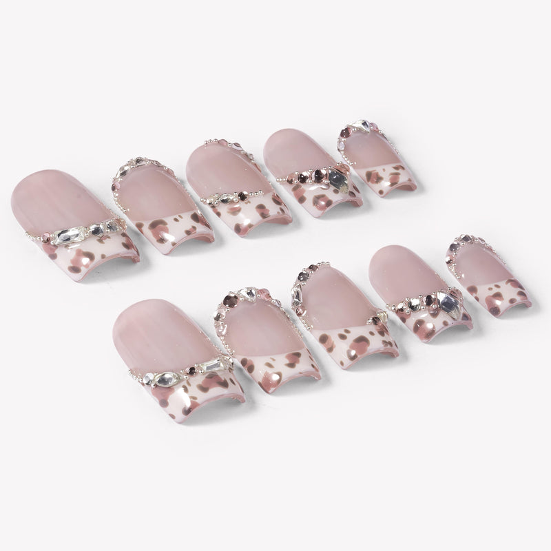 Flat lay of Sugar Kitten press-on nails with nude pink bases, leopard print French tips, and clear rhinestone accents